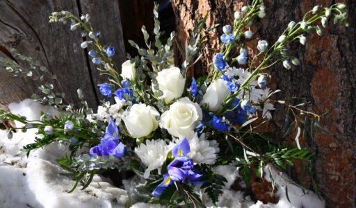 Formal blue and white flower arrangement in the snow next to a tree